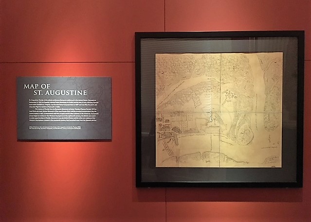 A color photograph of framed map depicting the Harbor of St. Augustine in 1595. An interpretive label is next to the framed map.