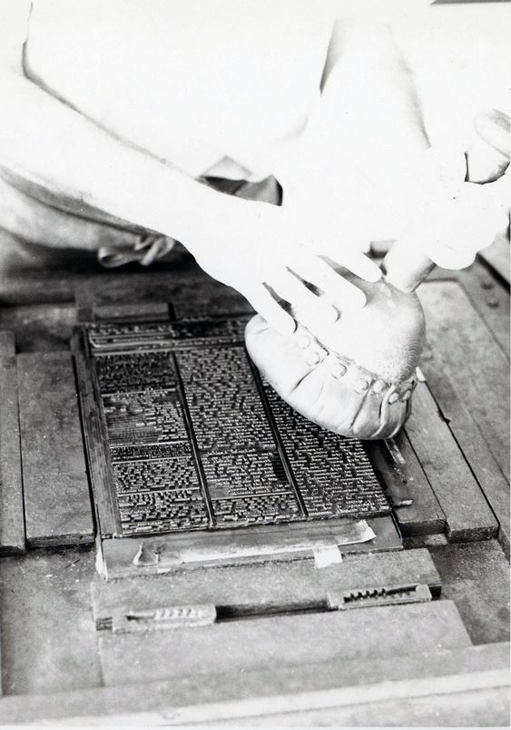 A black and white photograph of a person applying ink to a set type.