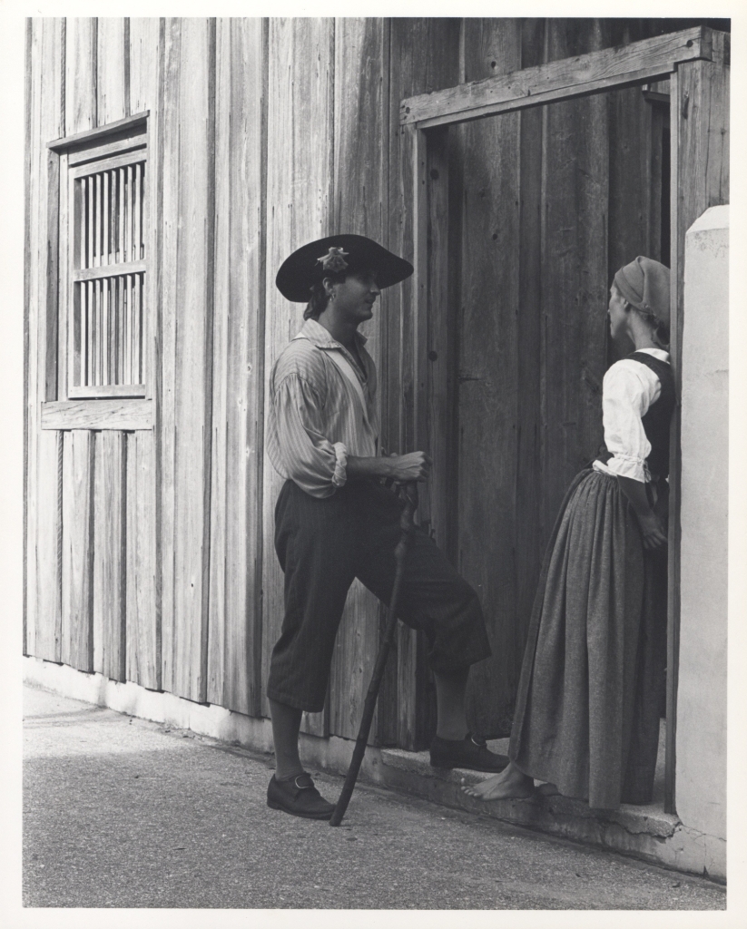 A black and white photograph of a man in Spanish Colonial inspired costume talking to a woman in Spanish Colonial inspired costume.